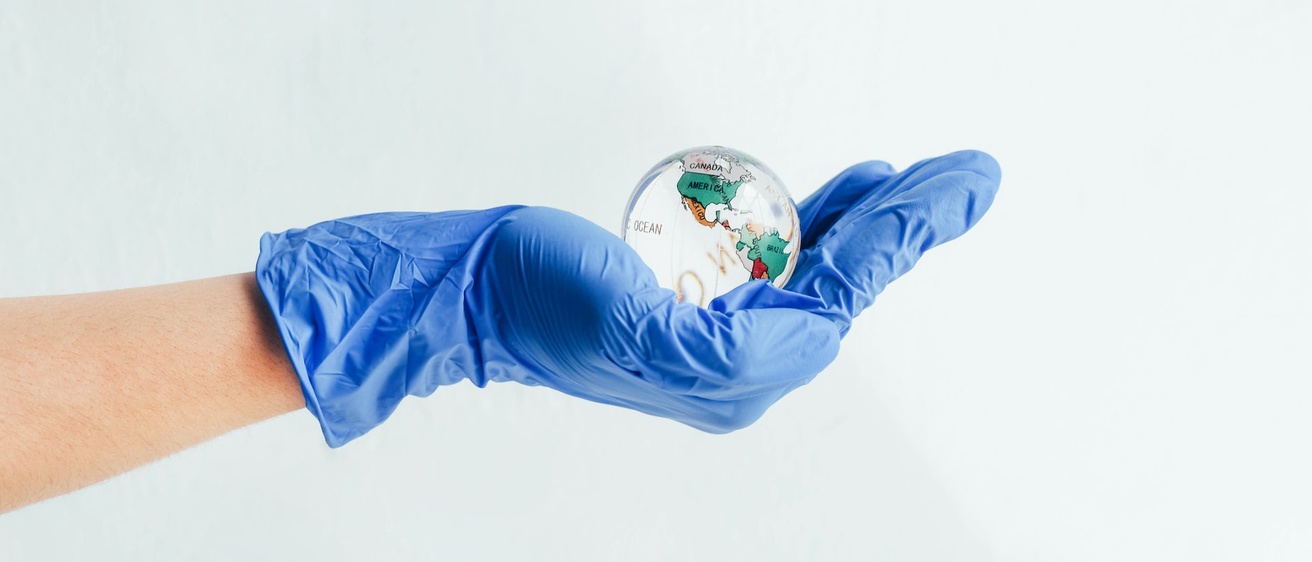 A hand in a blue latex glove holding a clear globe.