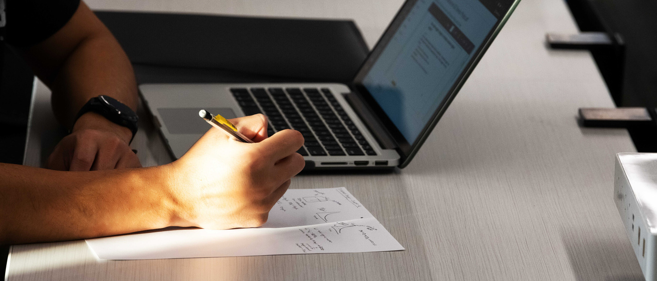 Person writing next to a open laptop