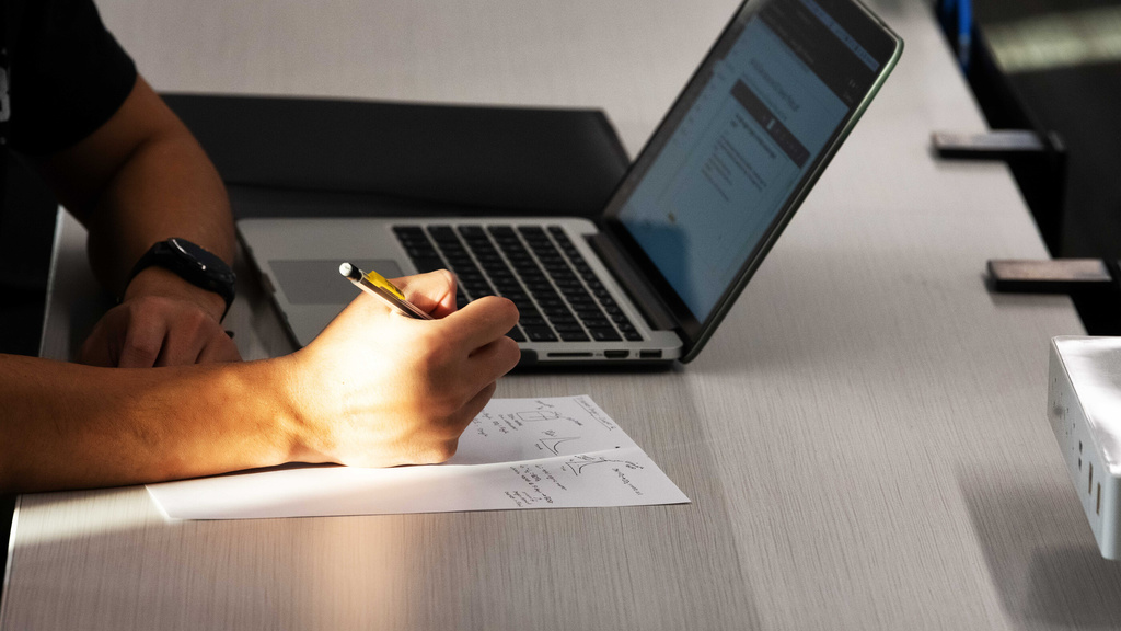 Person writing next to a open laptop